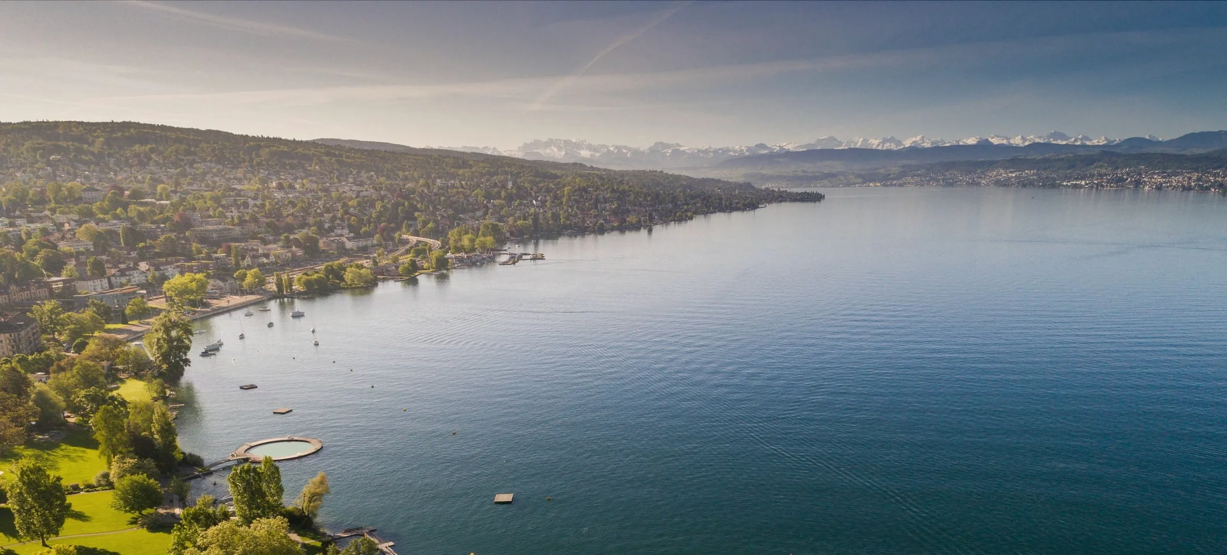 Aerial view of Lake Zurich with wooded shoreline villages and snowy Alps on the horizon
