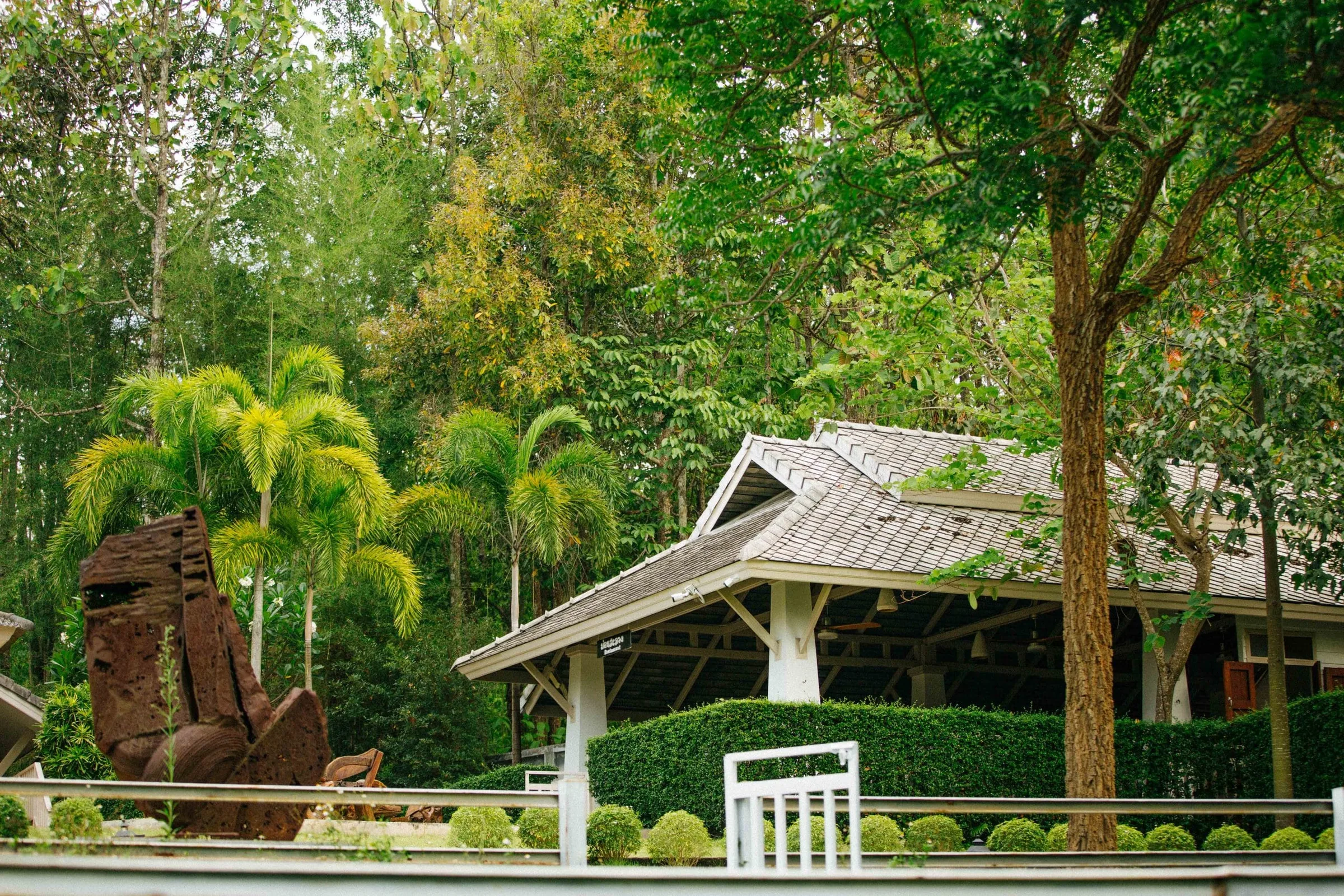 Open Thai sala pavilion with a pitched roof set among palms and tall trees on a trimmed lawn in Chiang Mai