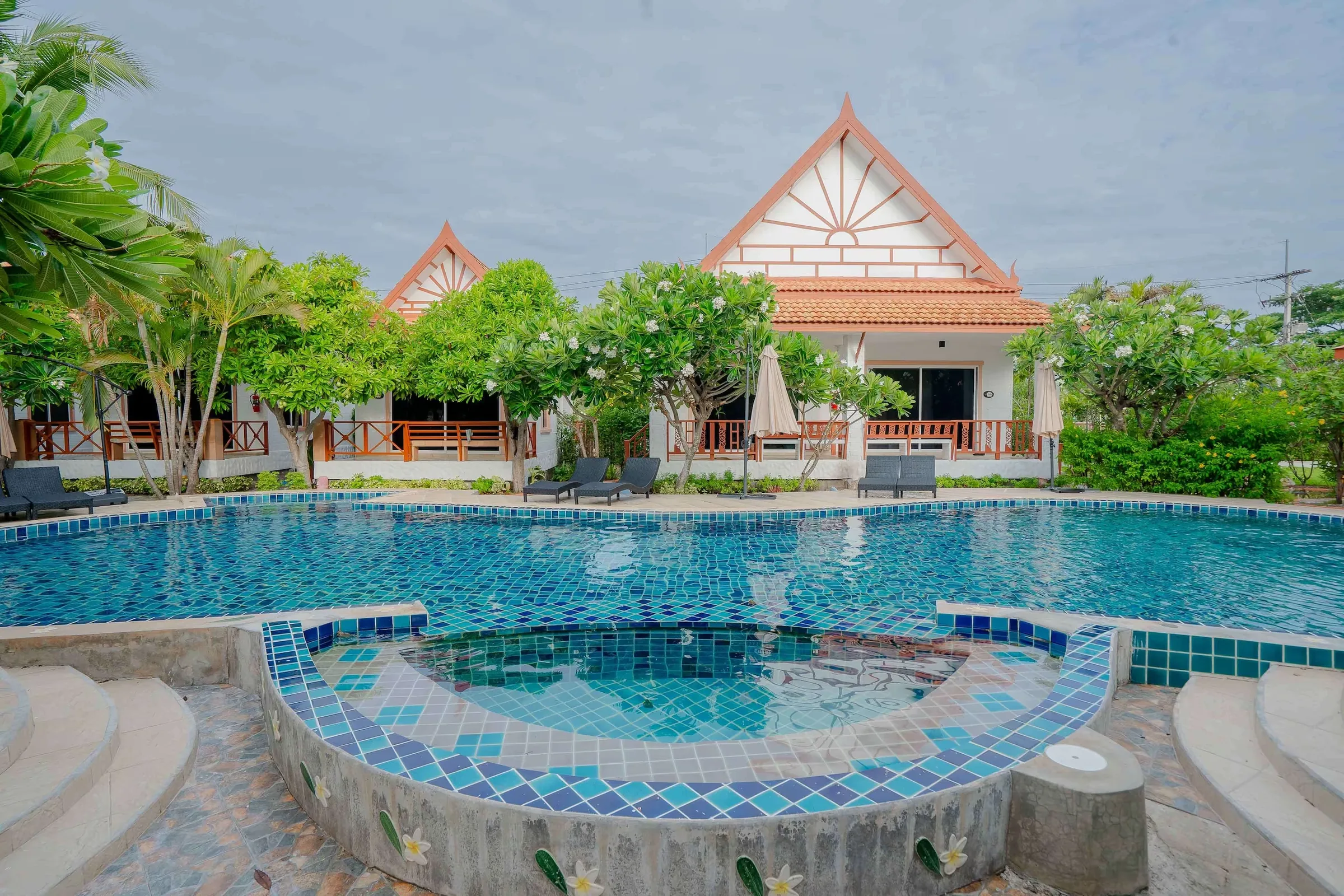 Swimming pool with a round tiled spa basin in front of bungalows with steep Thai gables and palms