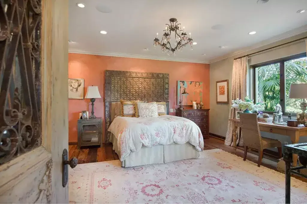 Bedroom with a coral accent wall, chandelier, floral bedding, desk and garden windows