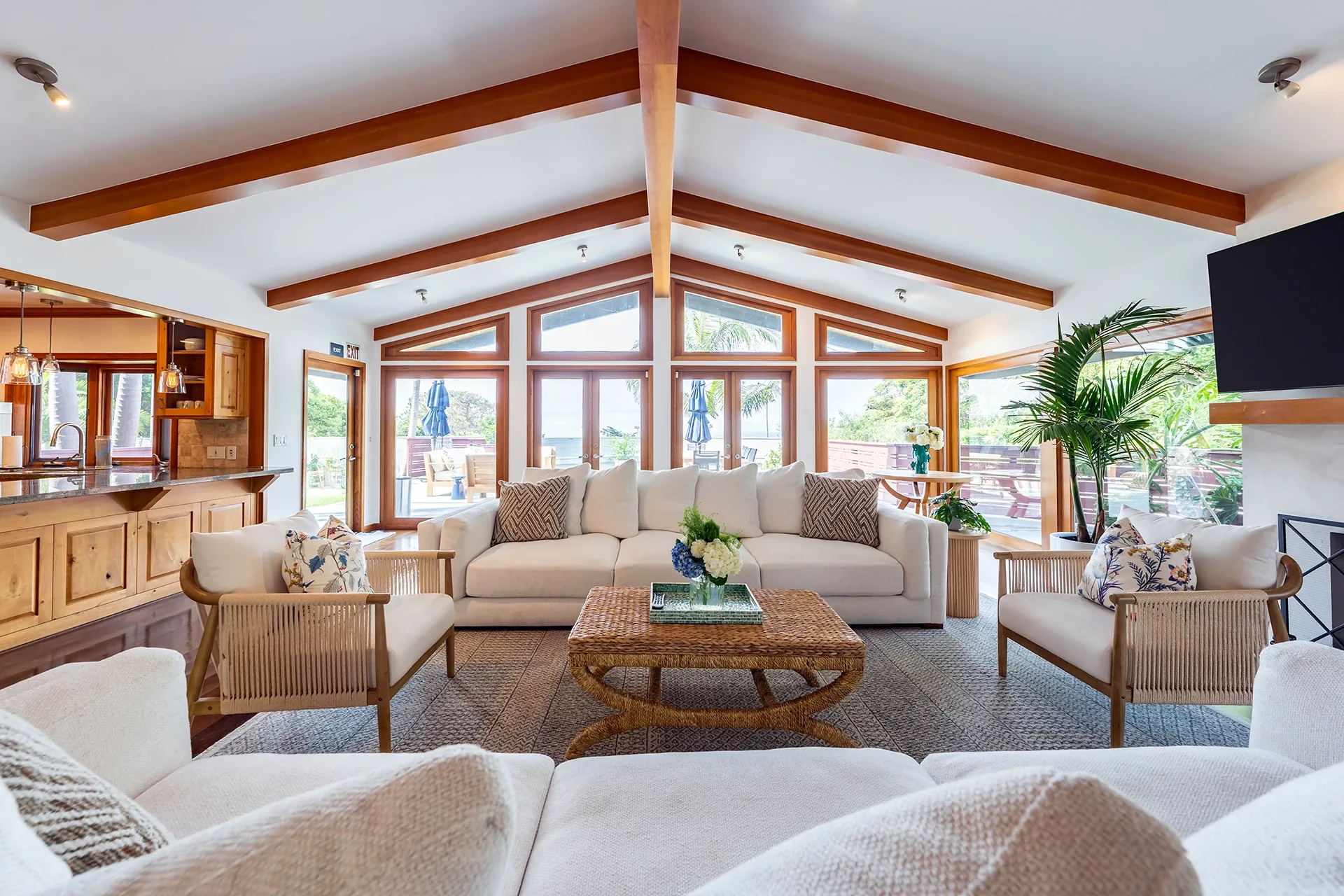 Living room with white sofas, rattan armchairs and a beamed vaulted ceiling with tall windows