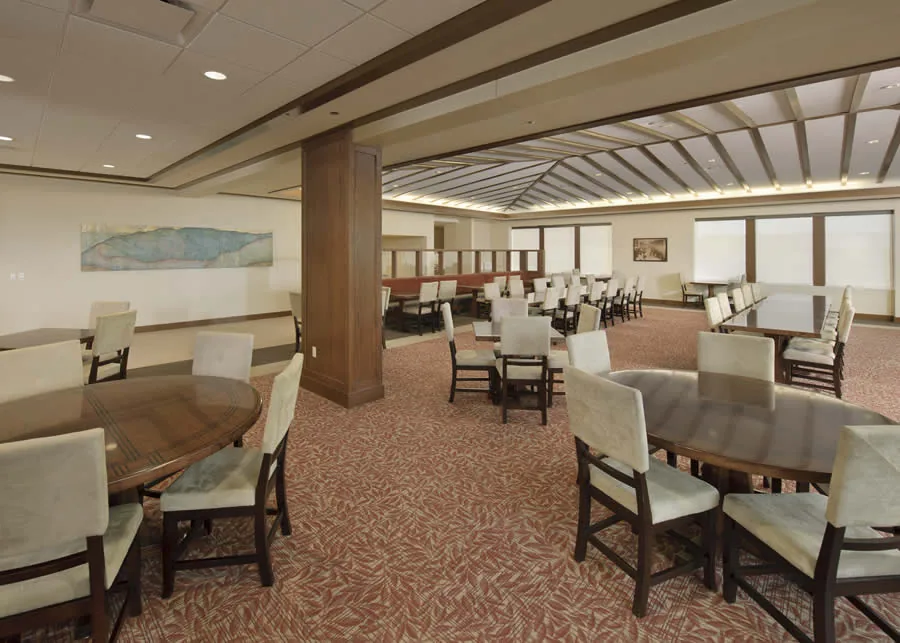 Dining room with round wooden tables, upholstered chairs and a timber-beamed ceiling