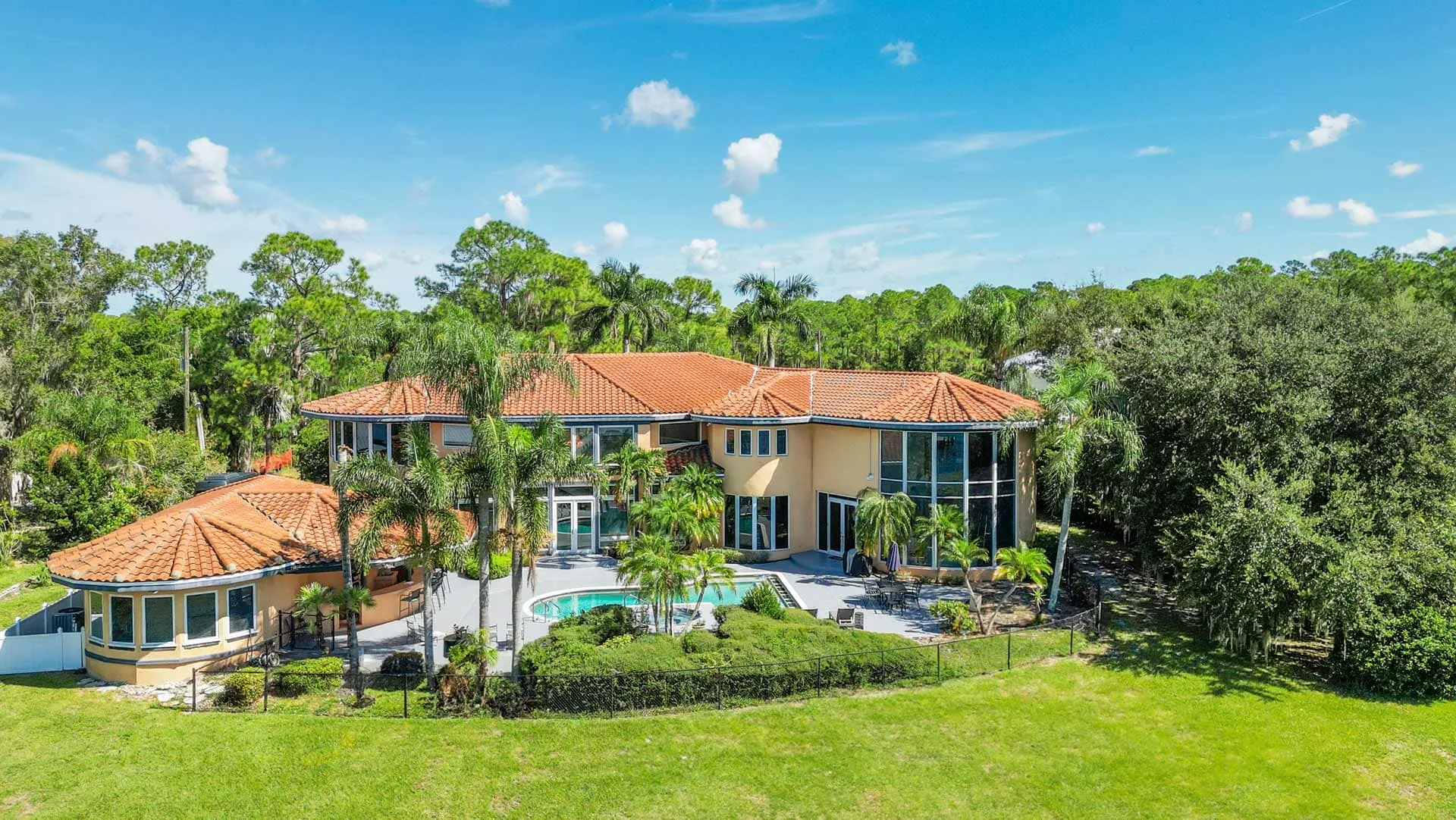Aerial view of the terracotta roofed main house with a pool, palm trees and lawn, backed by dense oak woodland