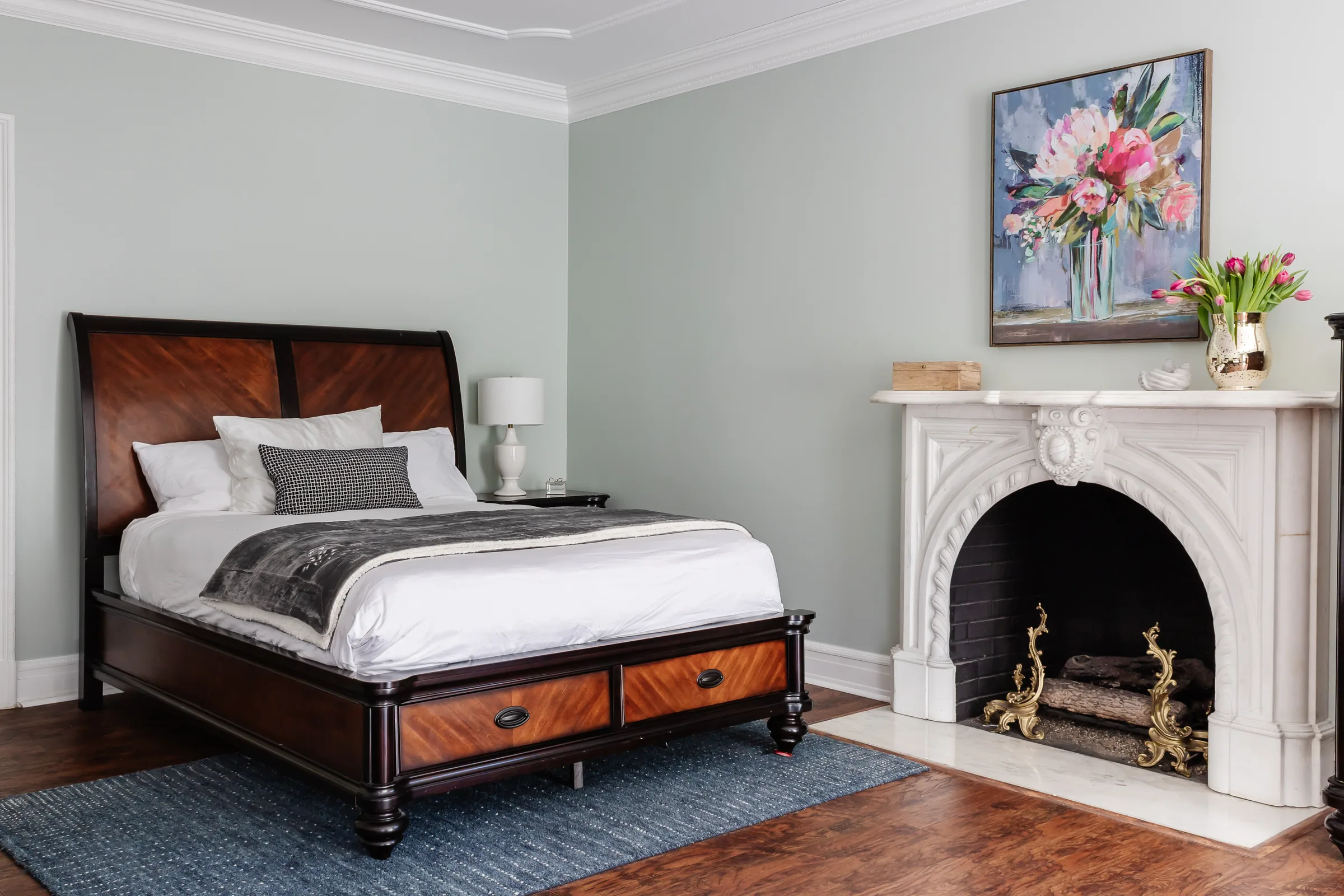 Guest bedroom with a dark wood bed, white bedding, a marble fireplace and a floral painting