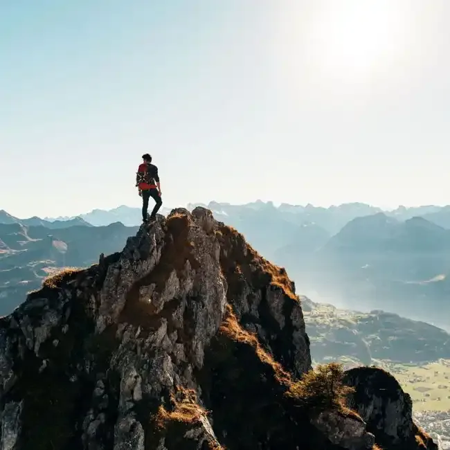 Hiker standing on a rocky summit above misty mountain ridges in early morning light