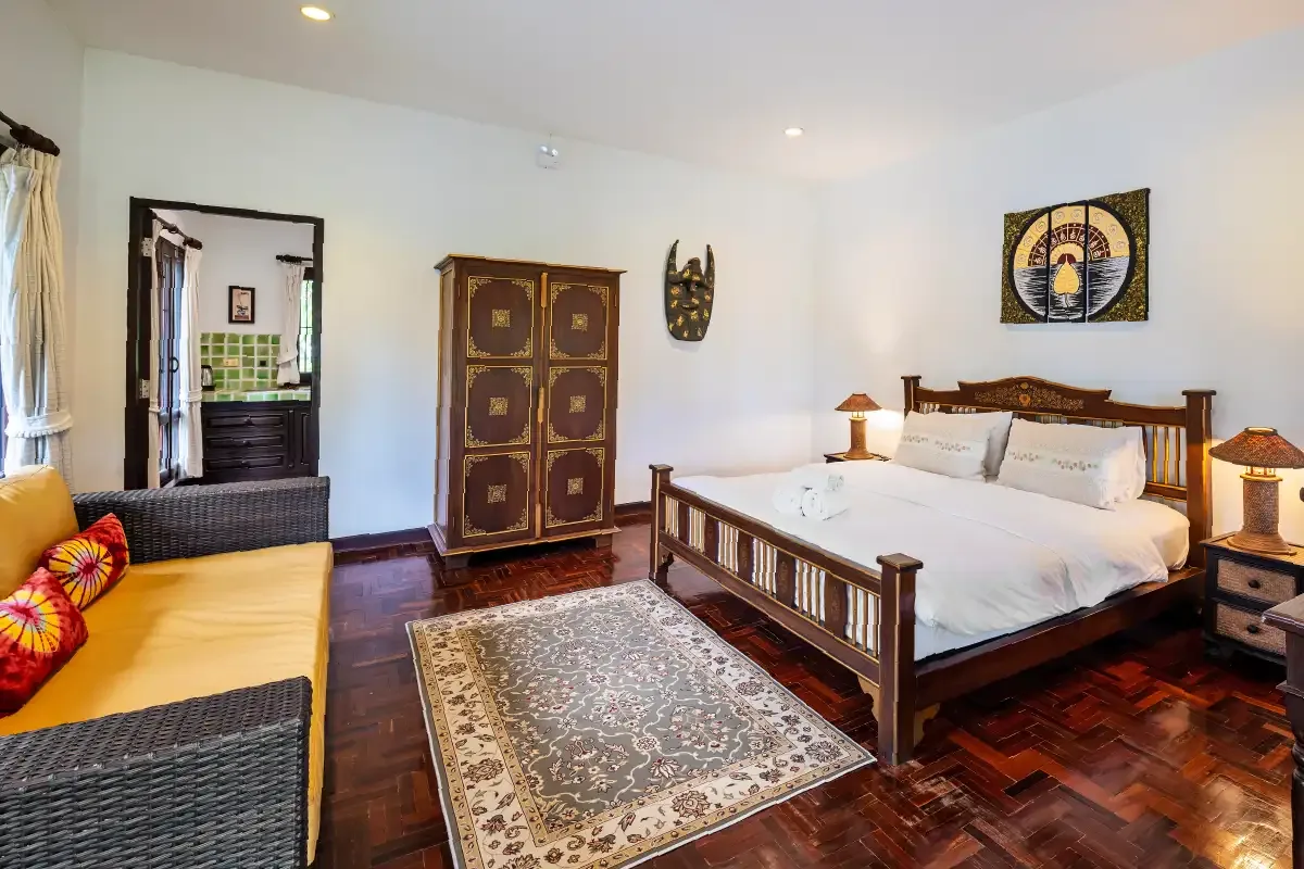 Bedroom with a carved wooden bed, dark wood floor, patterned rug, wardrobe and an orange daybed
