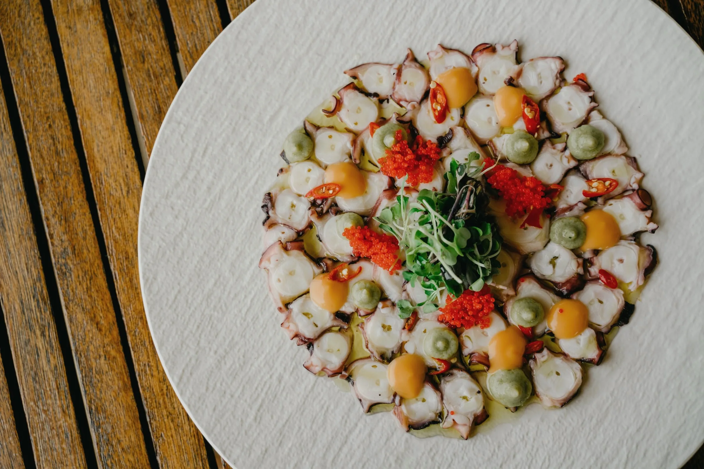Sliced octopus with herbs, olives and red garnish on a white plate on a wooden table