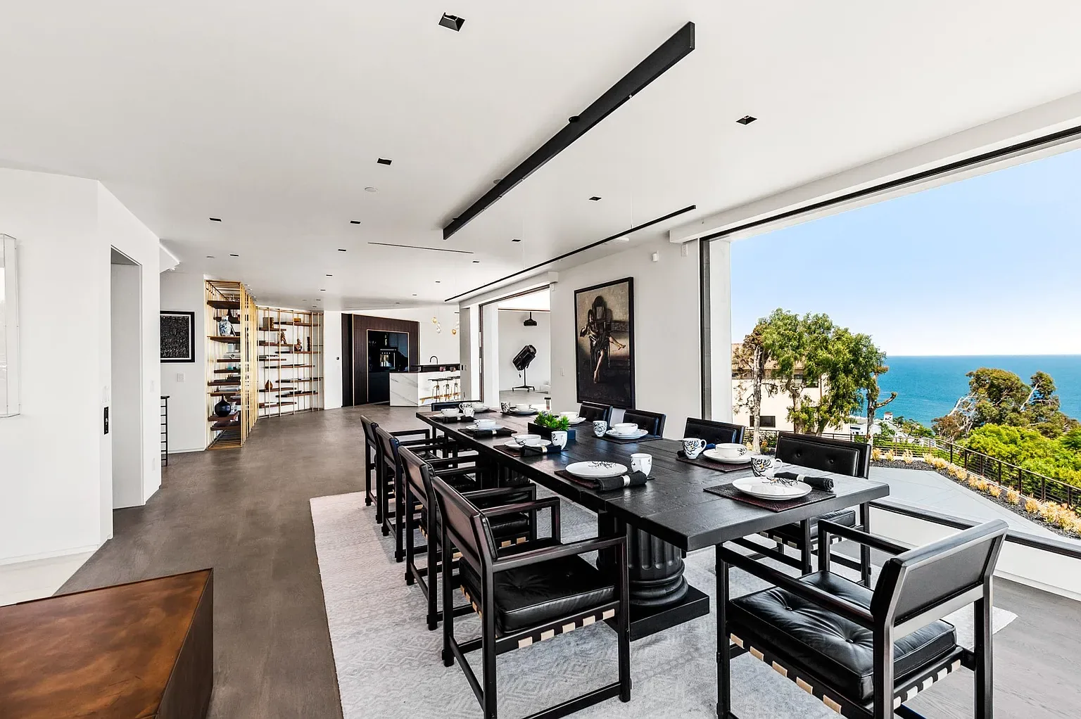 Long dining table with black chairs beside floor-to-ceiling windows looking out to the Pacific Ocean