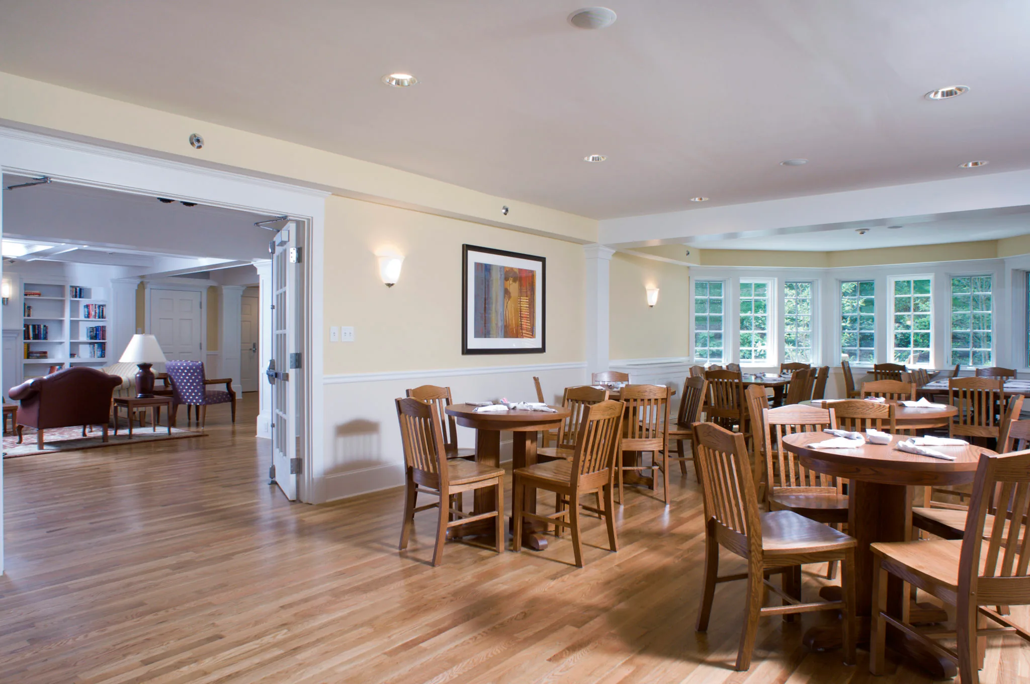 Bright dining room with wooden tables and chairs, oak floor and a row of windows