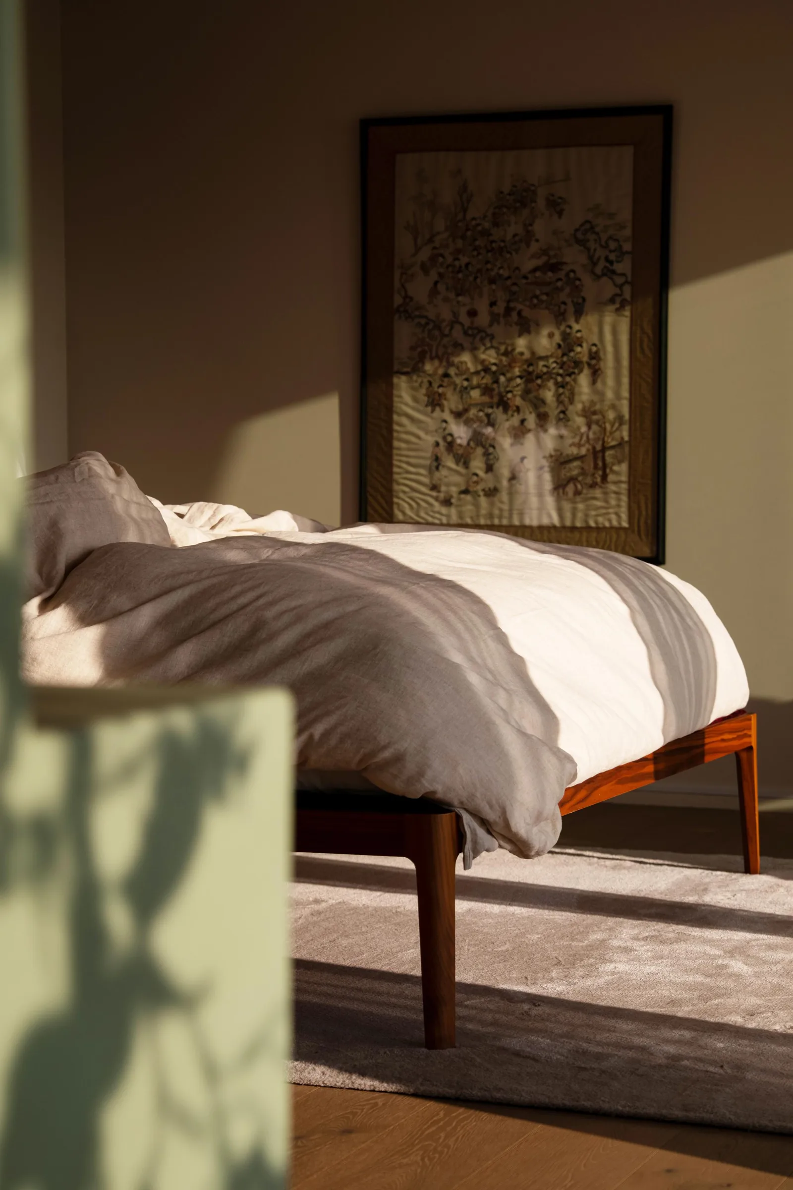 Villa bedroom with a wooden bed, crumpled white linen, a framed print and soft daylight