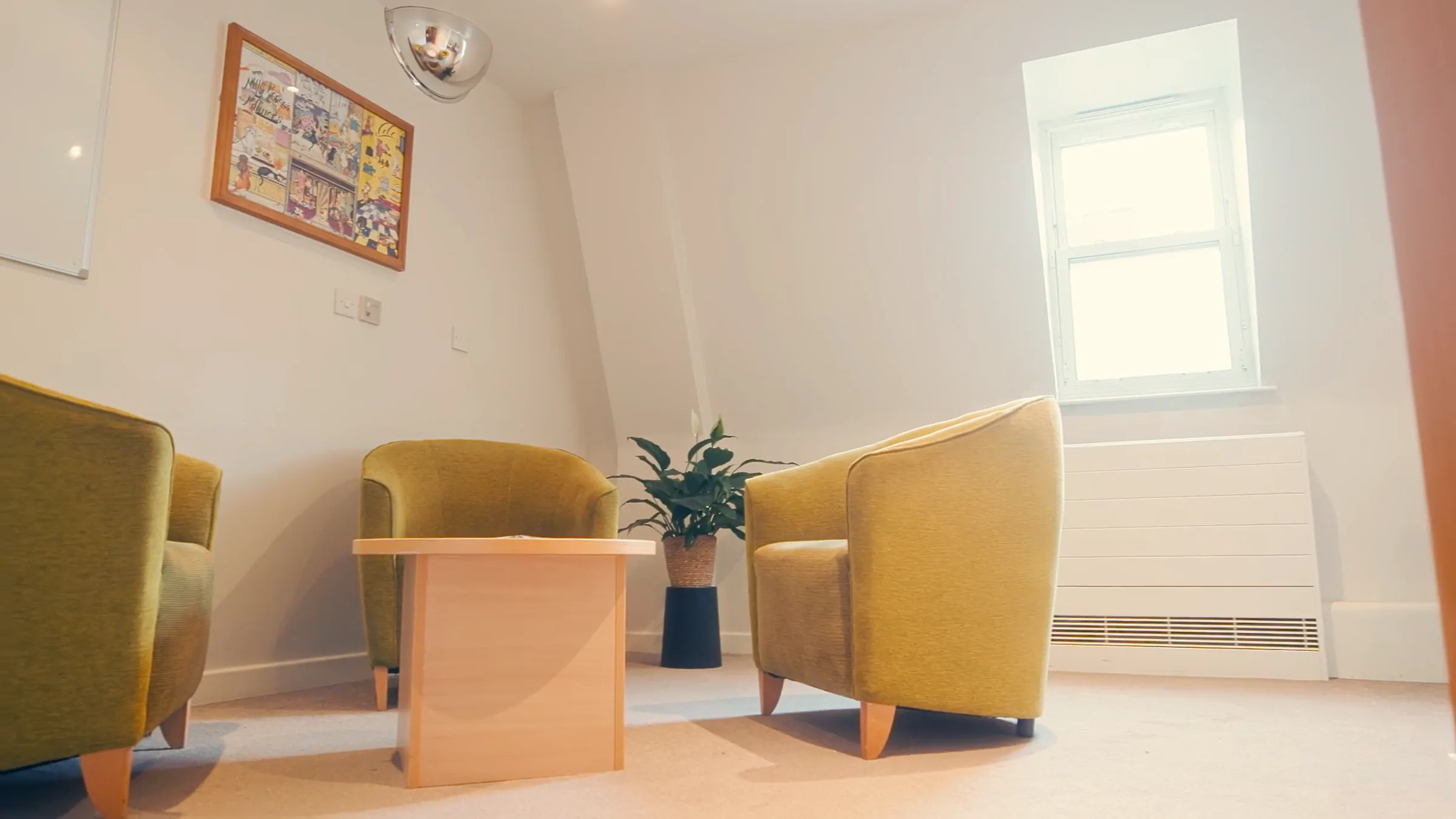 Small therapy room with two yellow armchairs, a low wooden table, a plant and a skylight window