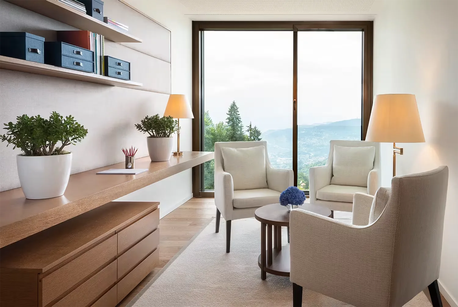 Consultation room with cream armchairs, a small round table and a full height window to the hills
