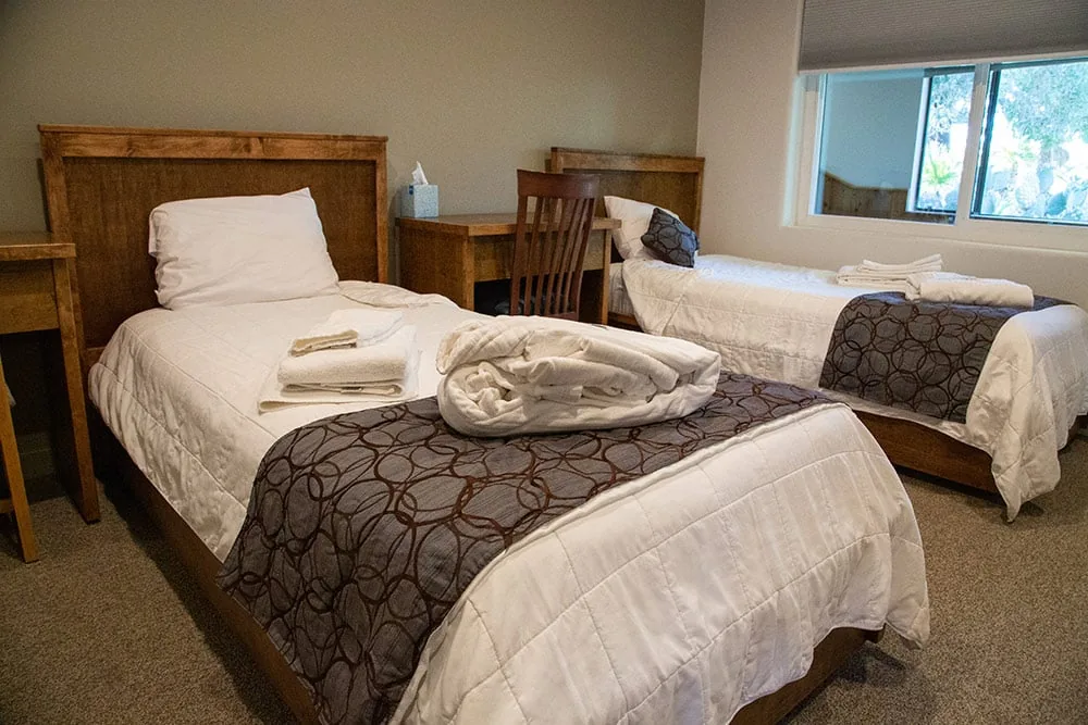 Client bedroom with two wooden-framed beds, patterned throws, folded towels and a window