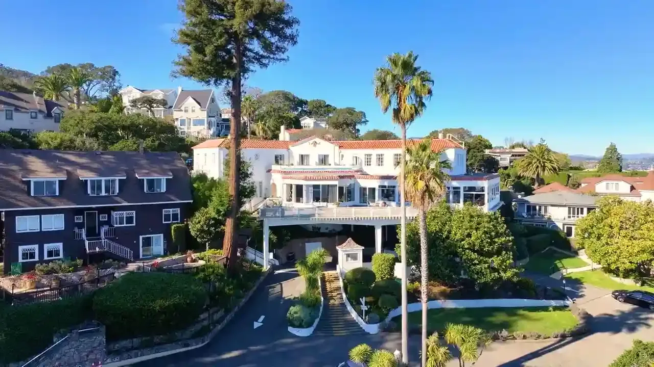Aerial view of the white historic main building with palm trees and residences on a Sausalito hillside