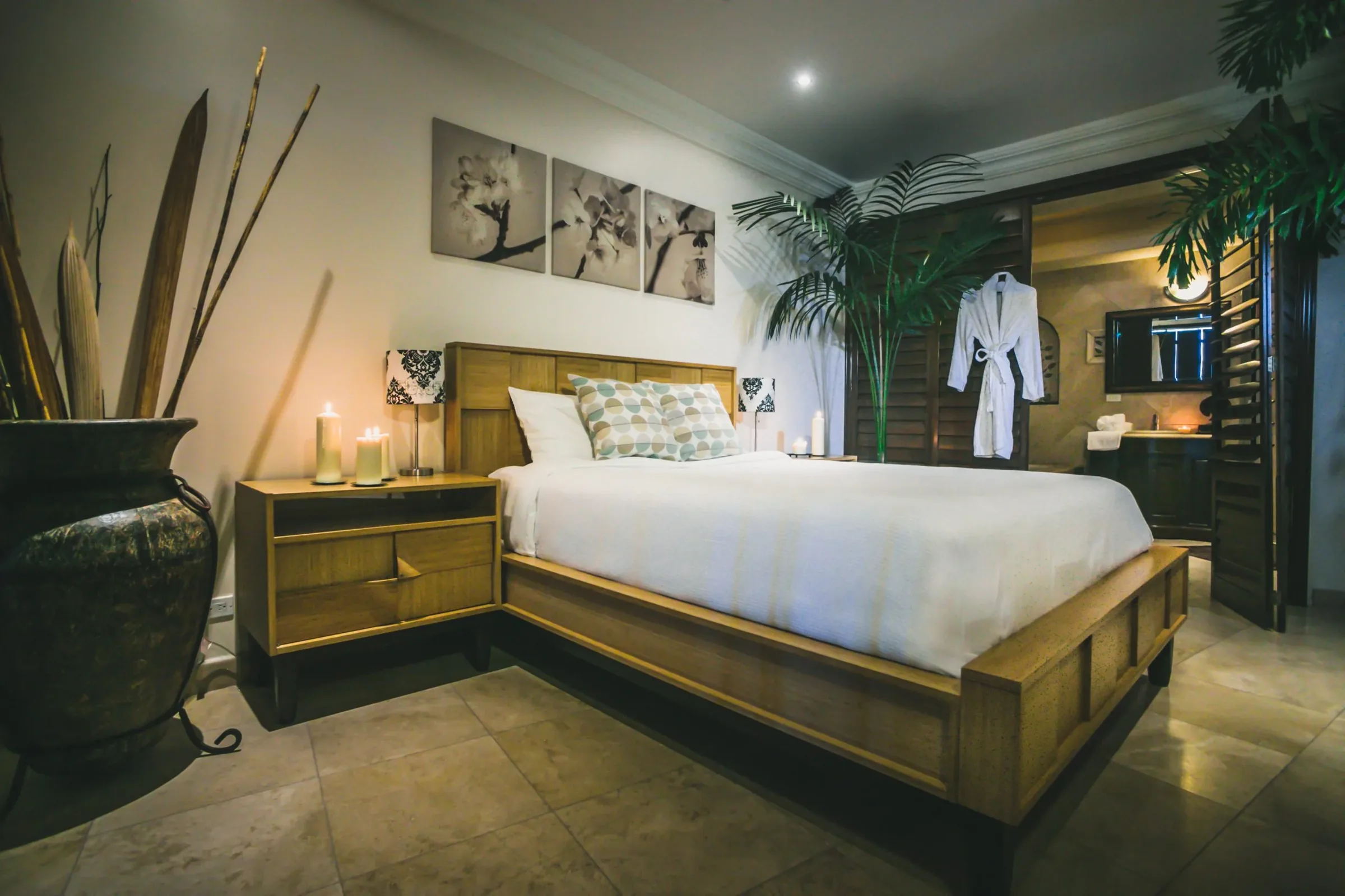 Master suite with a wooden double bed, white linen, lit candles, wall art and a hanging bathrobe