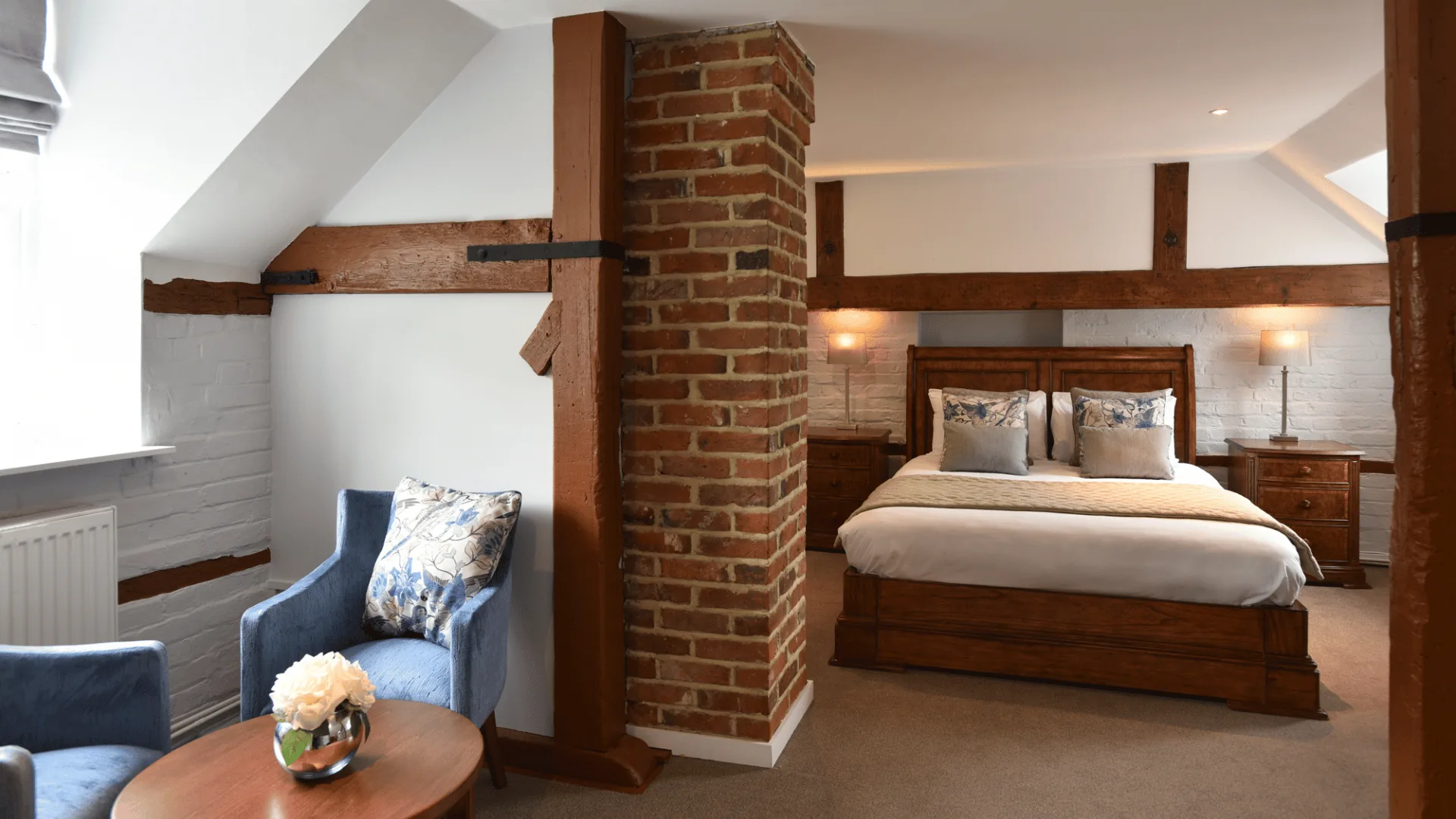 Bedroom with a brick chimney column, timber frame, double bed and blue armchair by a small table
