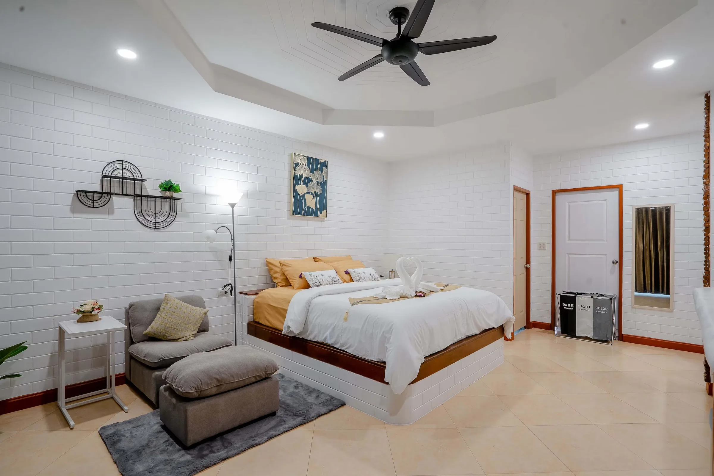 Bungalow bedroom with a double bed, grey armchair and footstool, ceiling fan and white brick walls