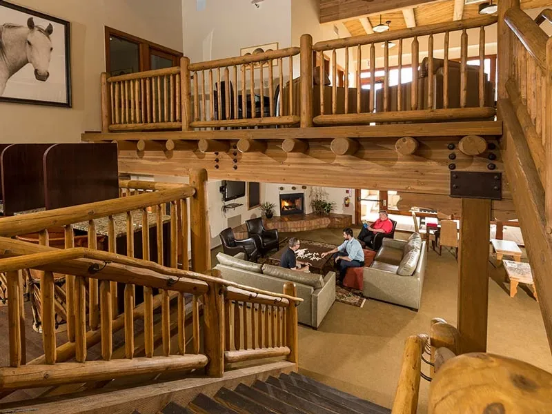 Lodge lounge with log railings, a wooden gallery level, sofas and people seated in the background