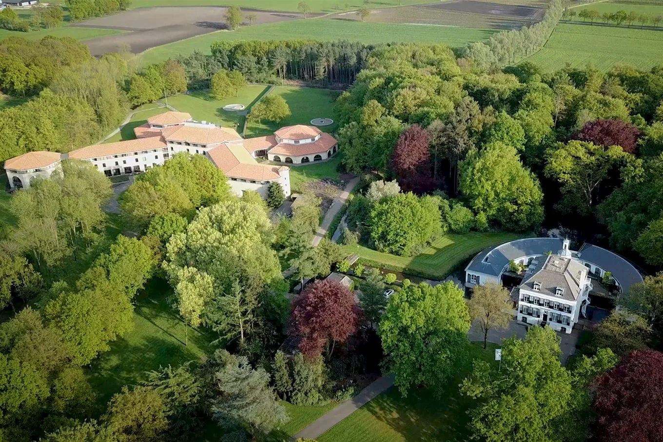 Aerial view of the white manor house and low clinic buildings among woodland, lawns and farmland