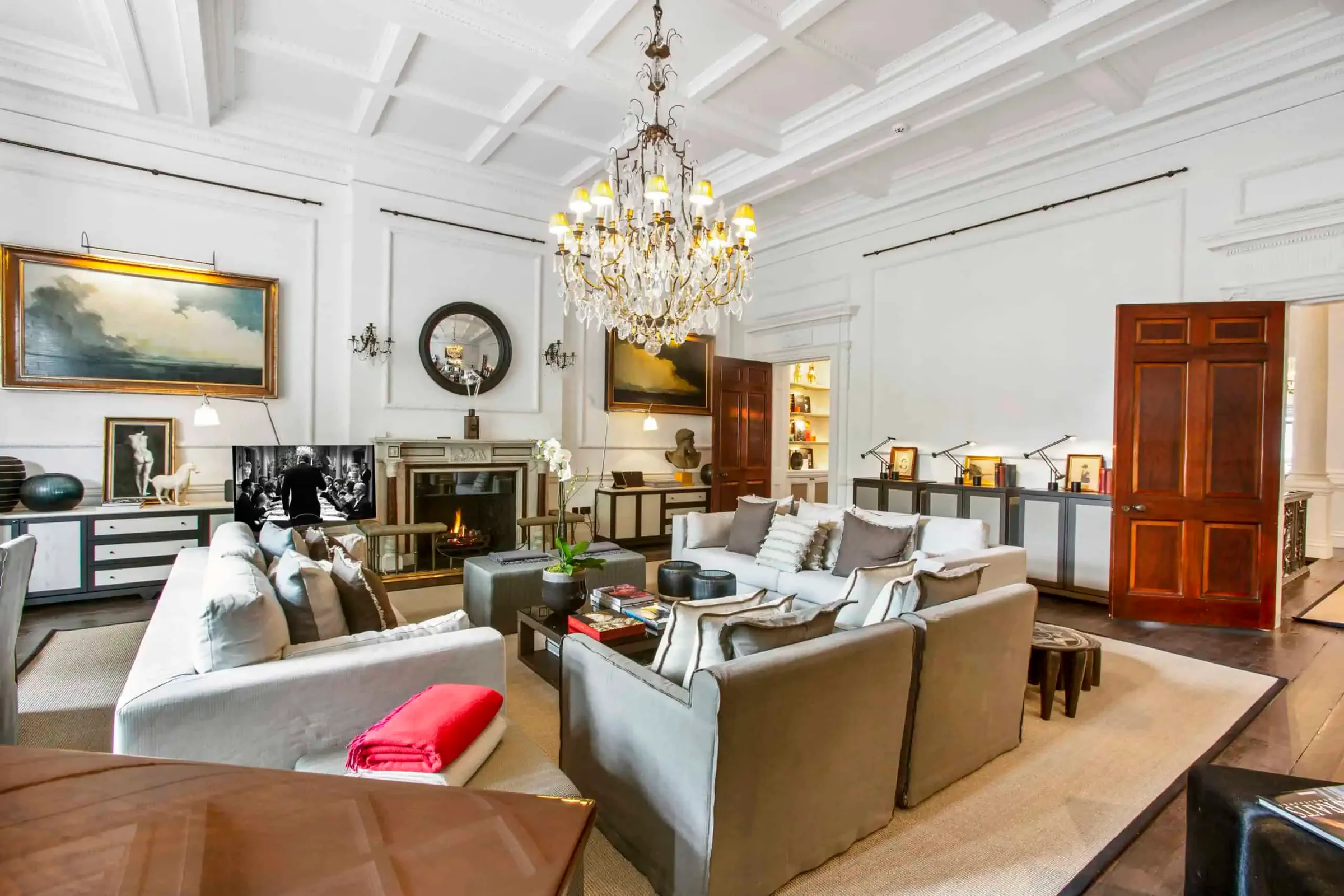 Large drawing room with grey sofas, a crystal chandelier, coffered ceiling and framed paintings