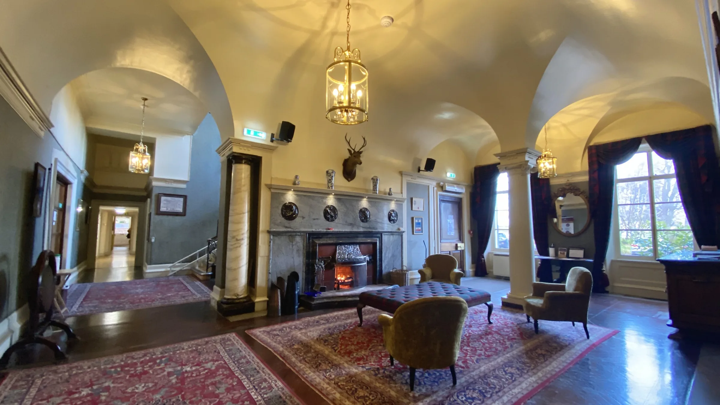 Vaulted front hall with lantern lights, a lit stone fireplace, armchairs and patterned rugs