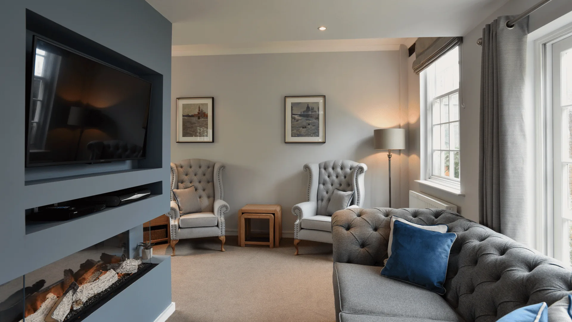 Living room with grey sofas, wingback chairs, a wall-mounted television and a modern fireplace