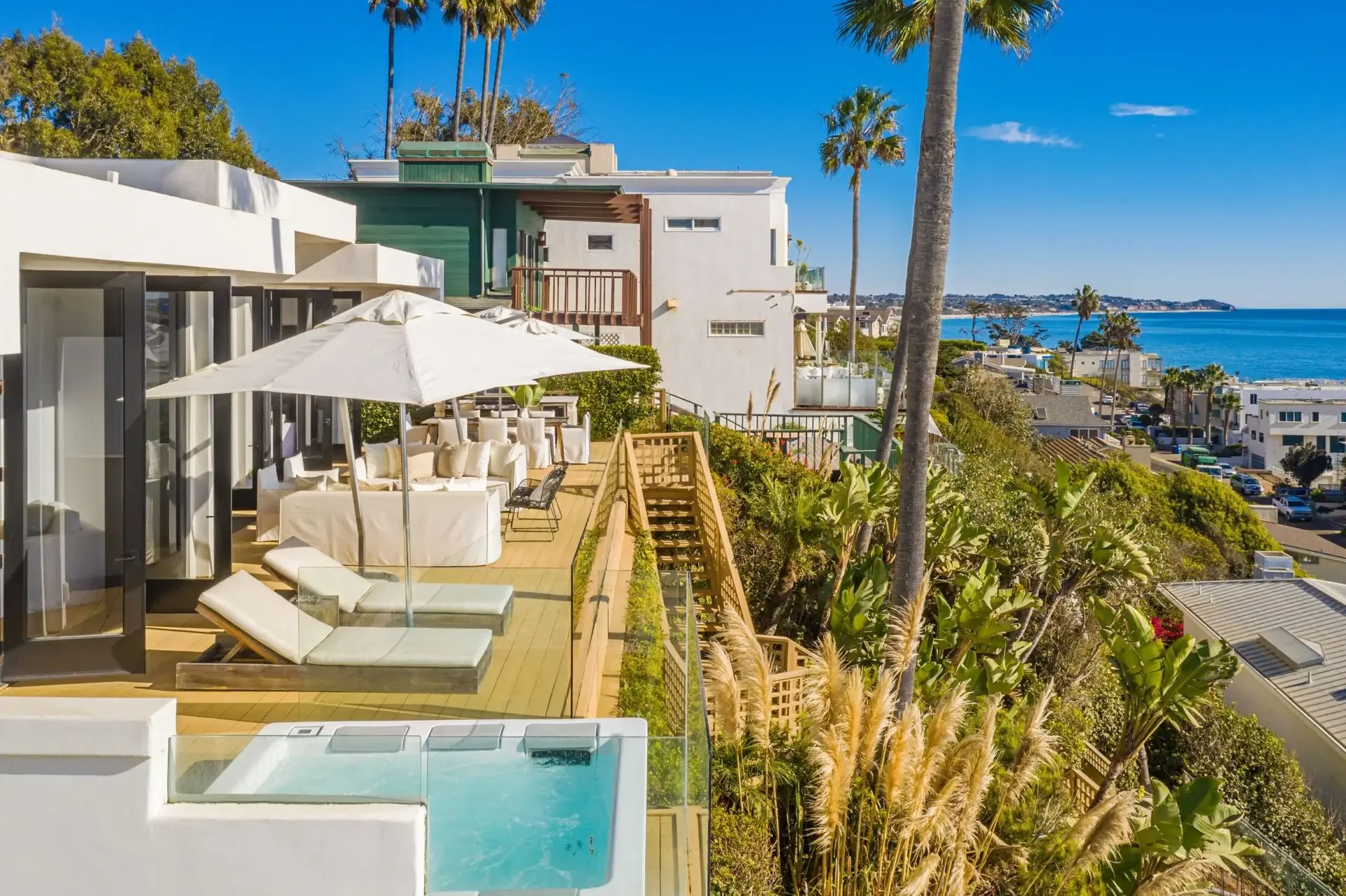 Hillside terrace with white umbrellas, loungers and a hot tub above palms and the Pacific coast