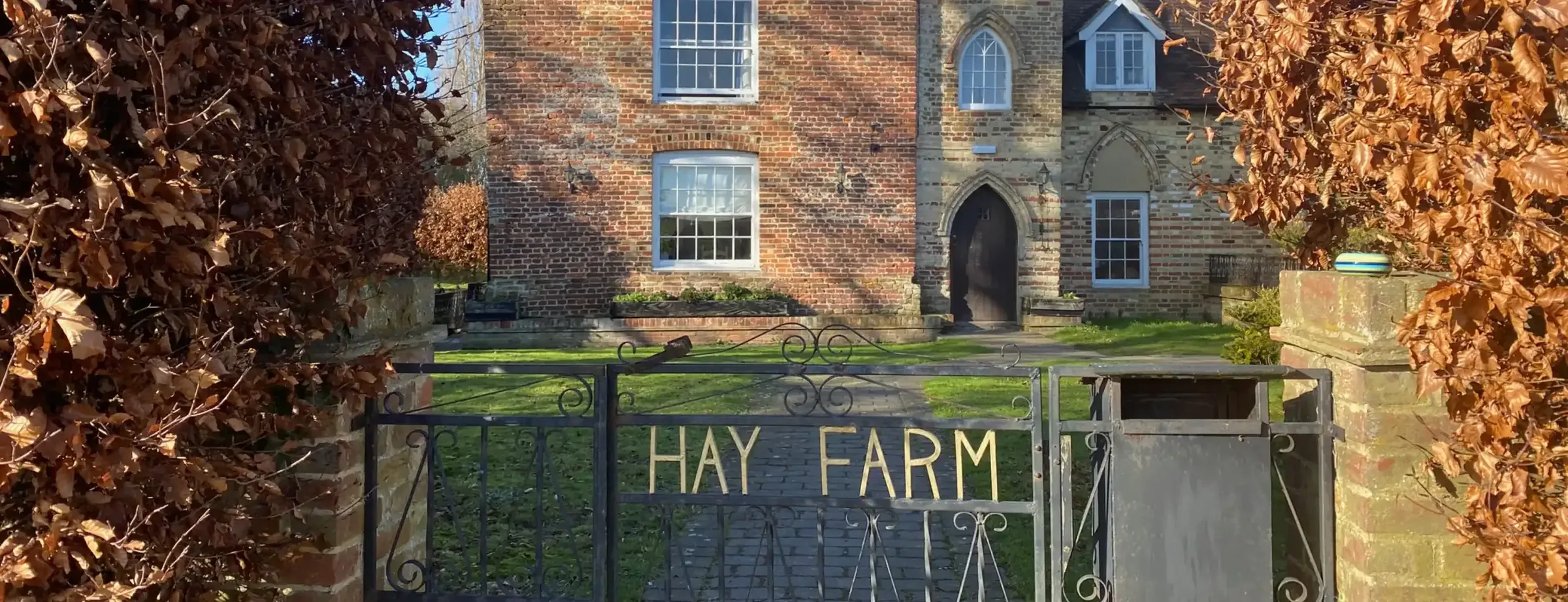 Iron gate with a Hay Farm sign in front of a brick house, framed by copper beech hedges