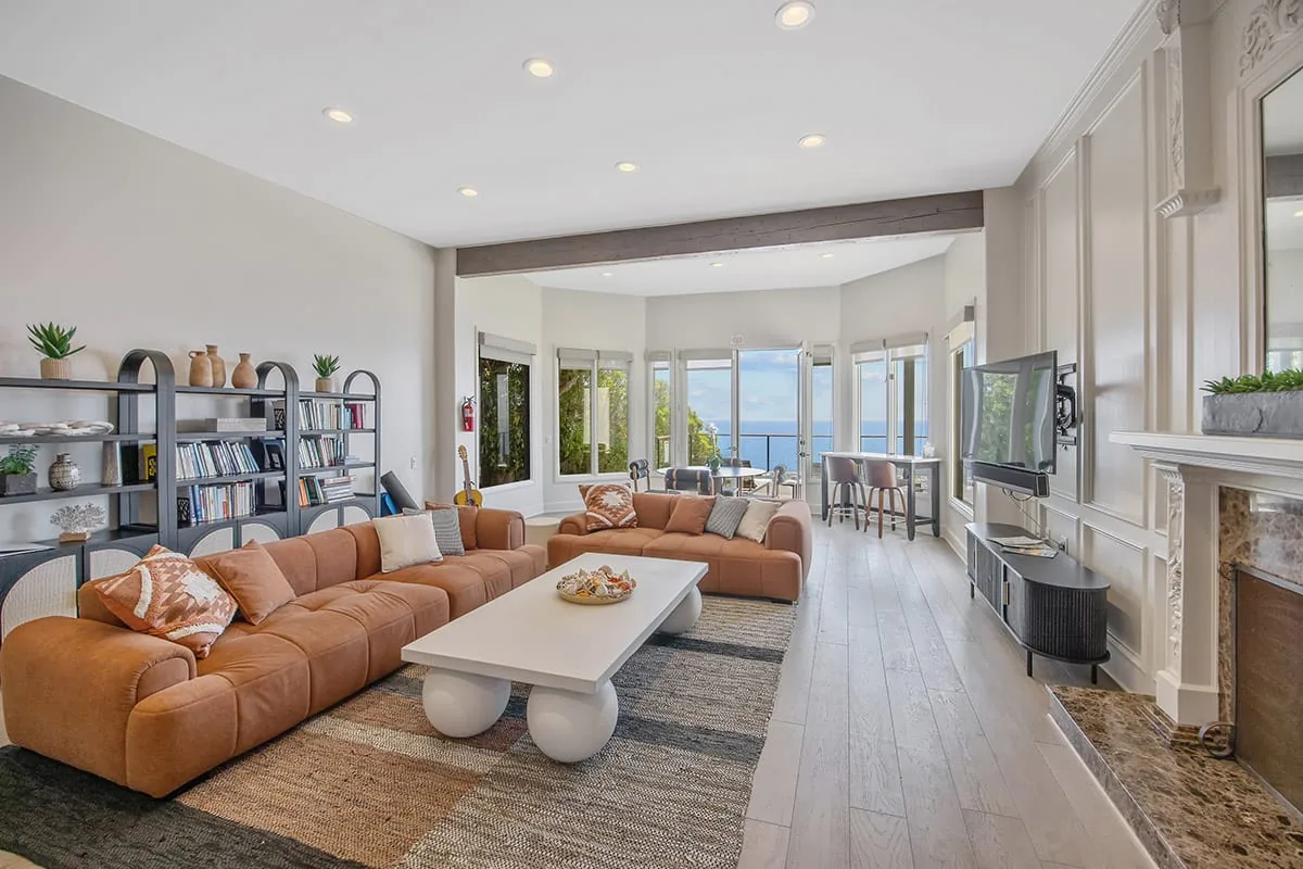 Communal living room with orange sofas, a white coffee table, bookshelves and bay windows