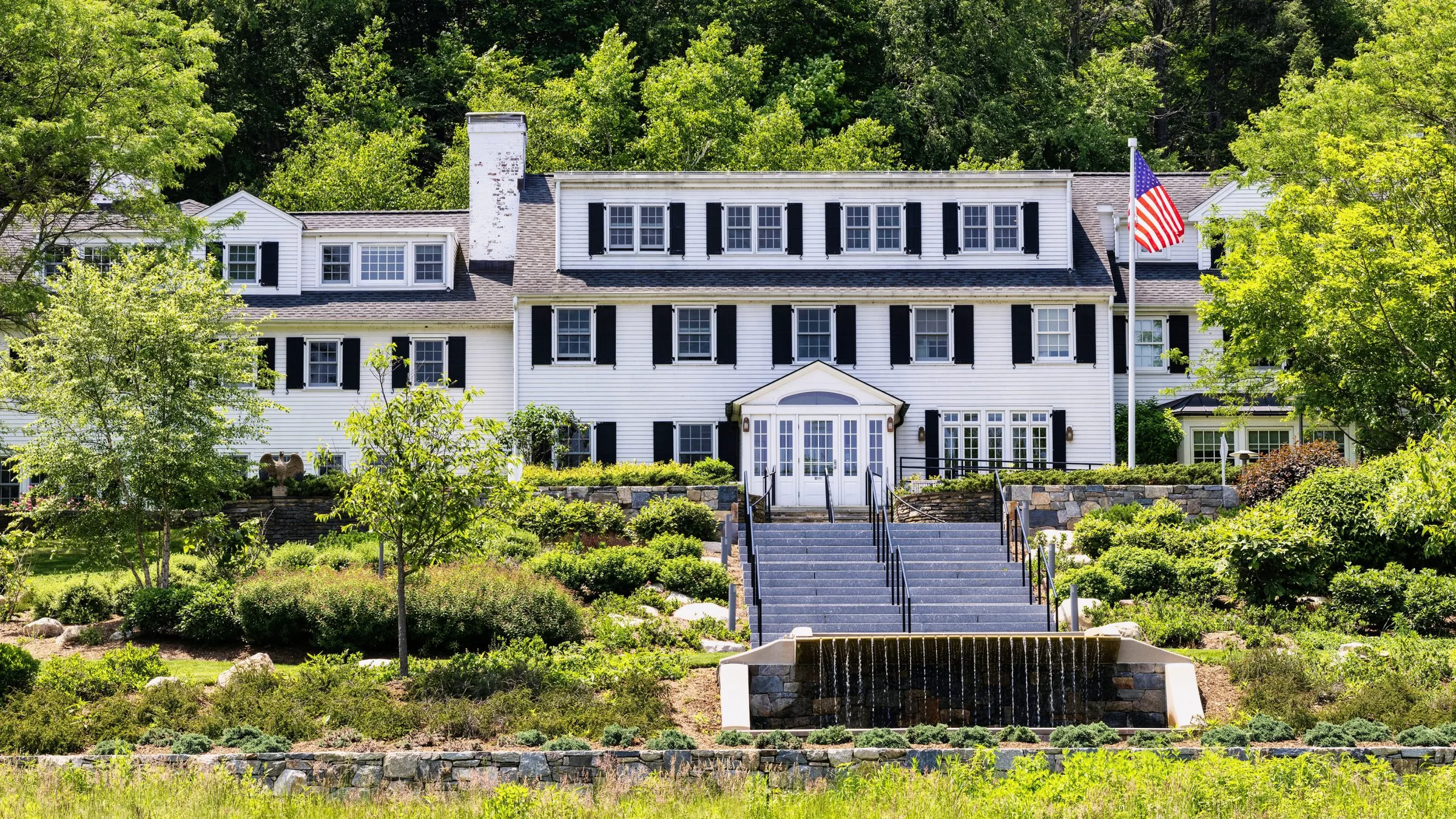 White colonial Main House with black shutters above terraced gardens and a central stone stairway