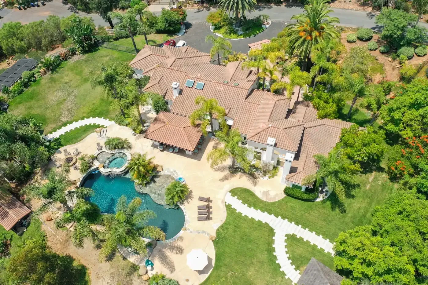 Aerial view of a tile-roofed house with a curved pool, lawns, palms and a winding garden path