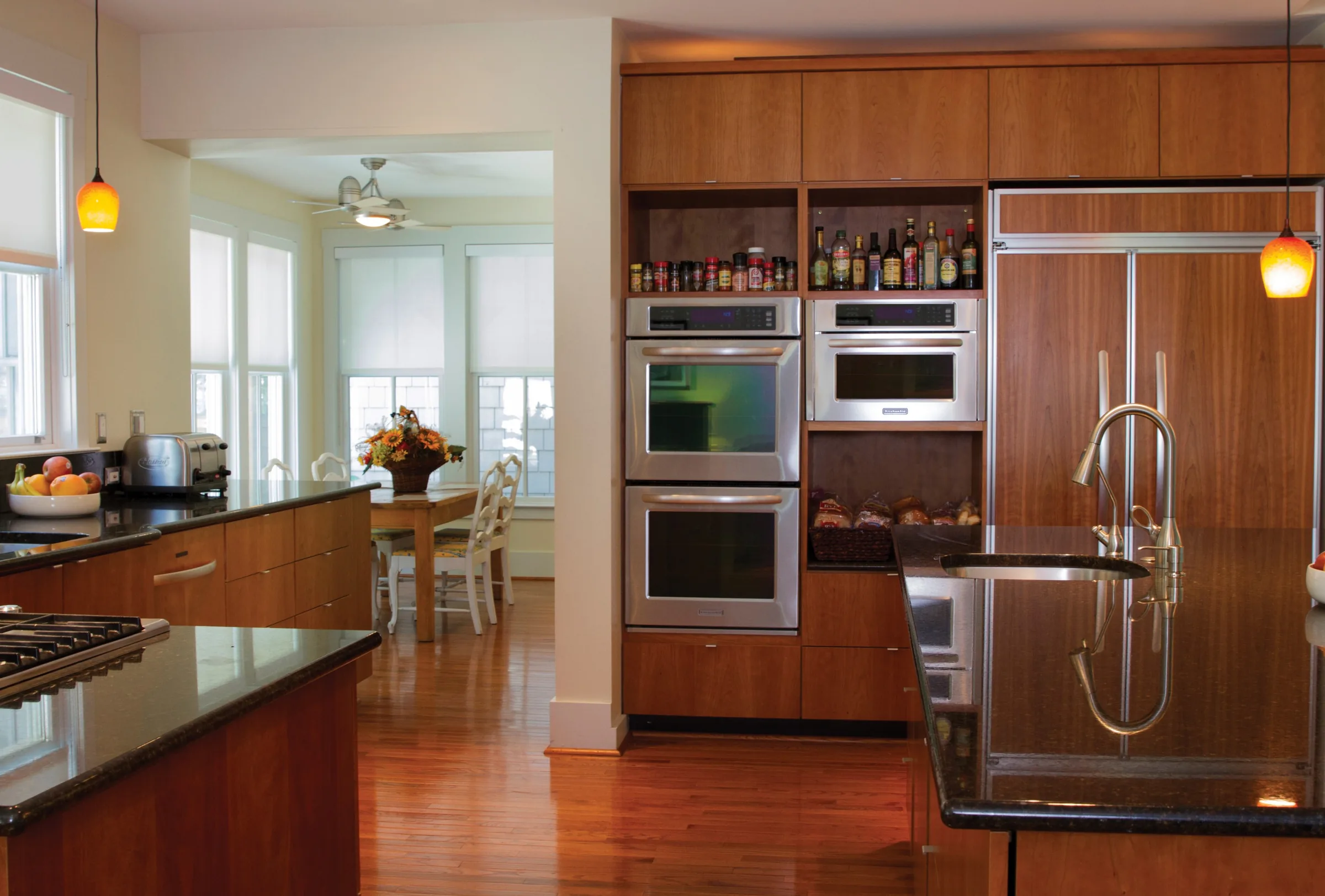 Kitchen with cherry wood cabinets, built-in double ovens, a dark stone island and pendant lights
