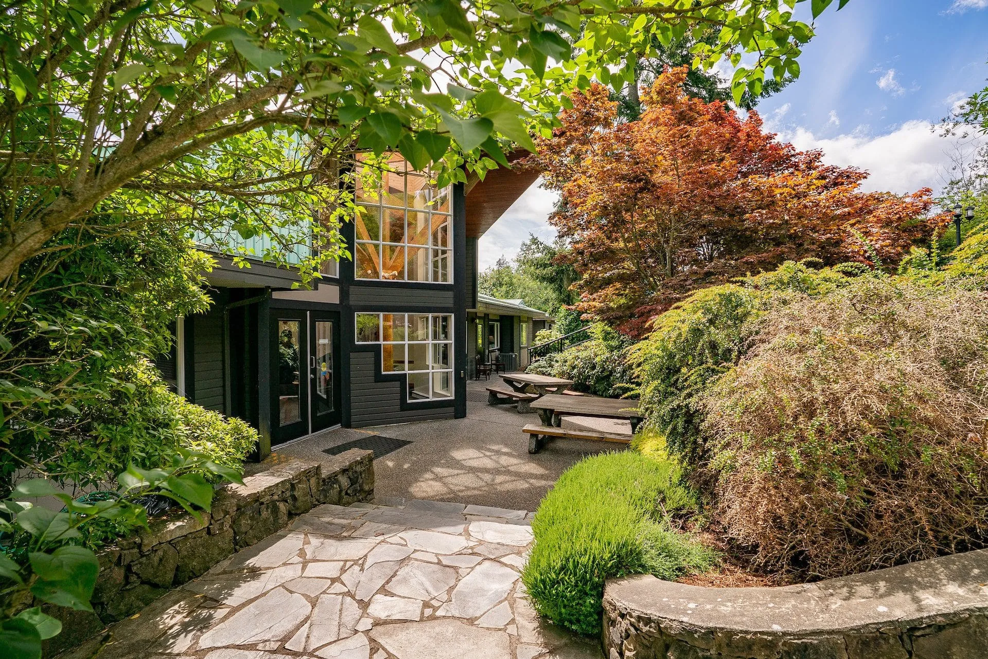 Flagstone path through planted gardens and red Japanese maples leading to a glazed building entrance