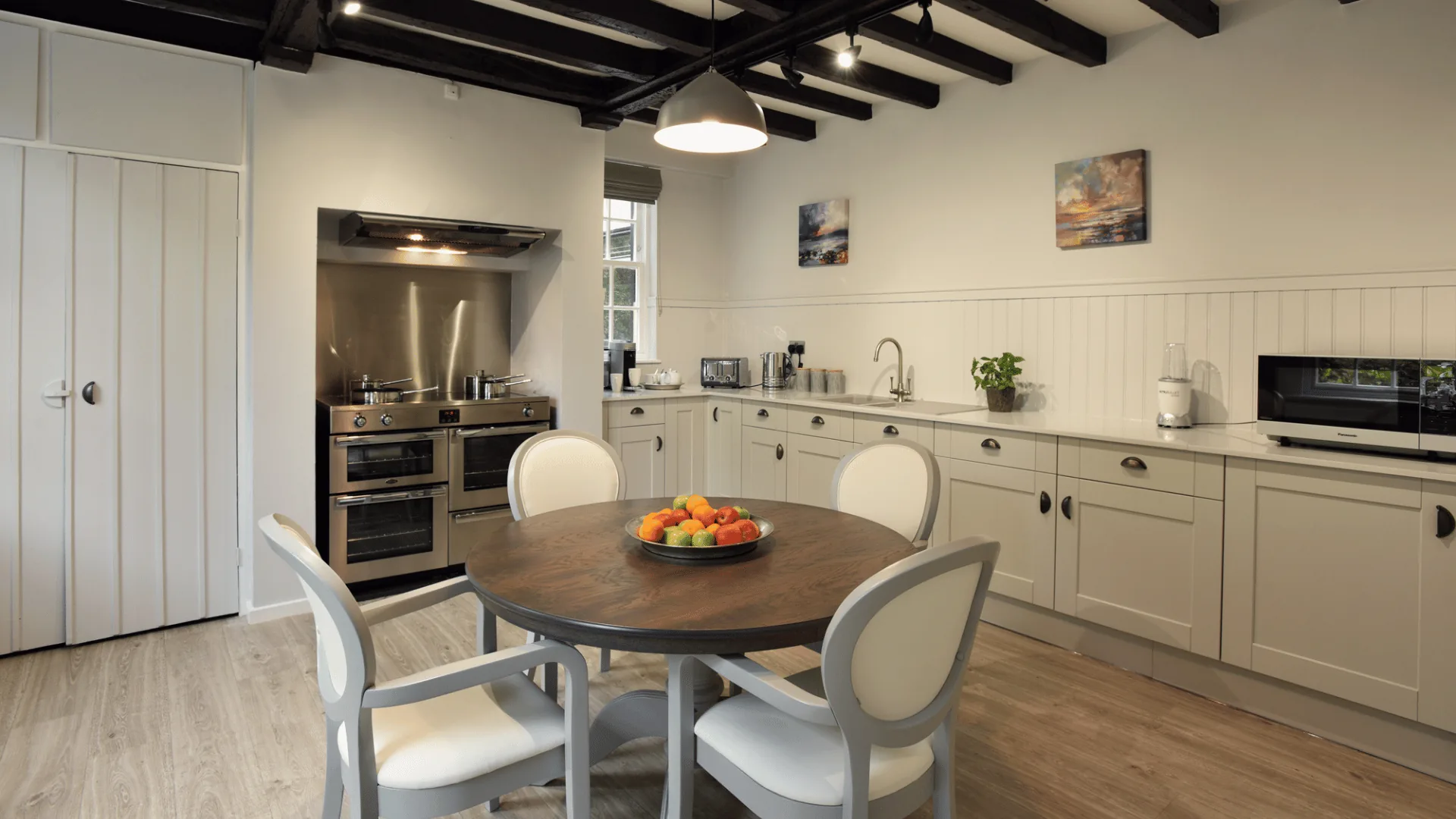 Cream kitchen under dark ceiling beams with a range cooker and a round dining table with four chairs