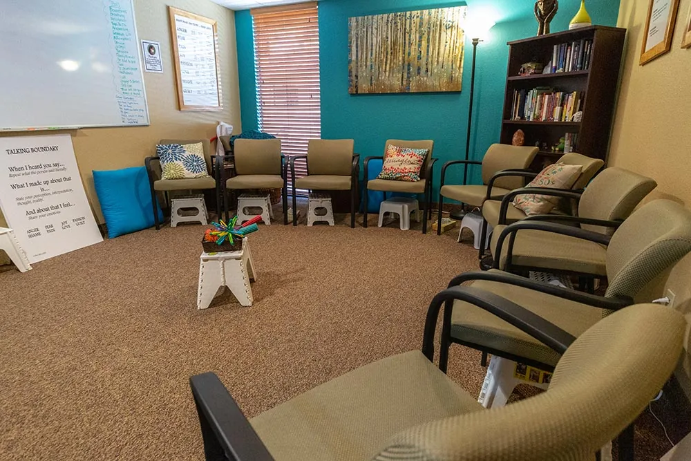 Group therapy room with a circle of padded chairs, a turquoise wall, bookshelf and whiteboard