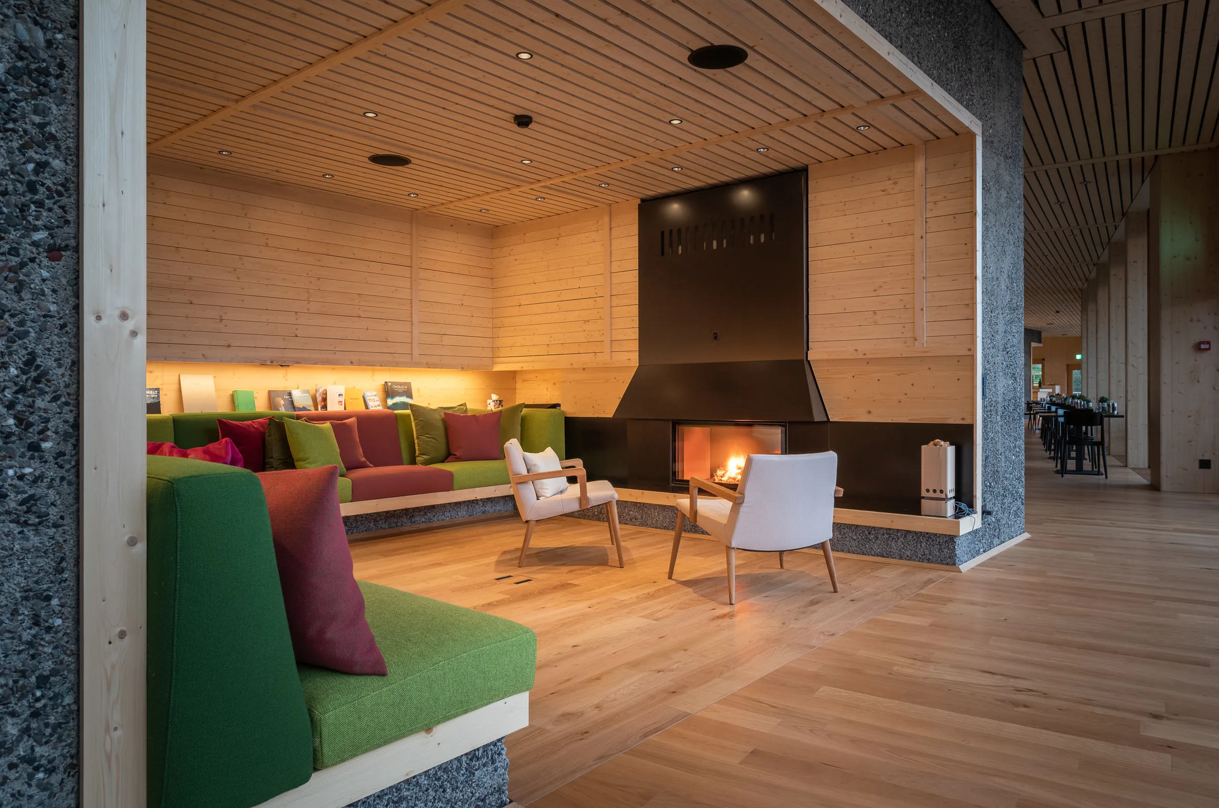Timber-lined lounge with a green corner sofa, armchairs, bookshelves and an open fireplace