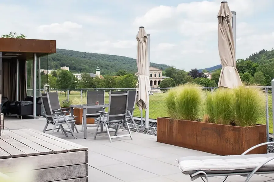 Rooftop terrace with parasols, garden chairs, sun loungers and grass planters overlooking wooded hills